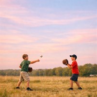 Two boys playing catch in a field at sunset